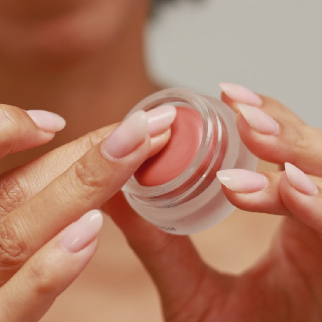 Woman applying Eco By Sonya Cream Blush to cheeks with finger, showing soft natural glow and smooth blendable texture.